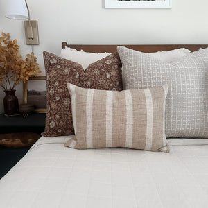 Agnes, Esme, and Caspian lumbar pillow covers on a white bed with rust floral arrangement on side table.