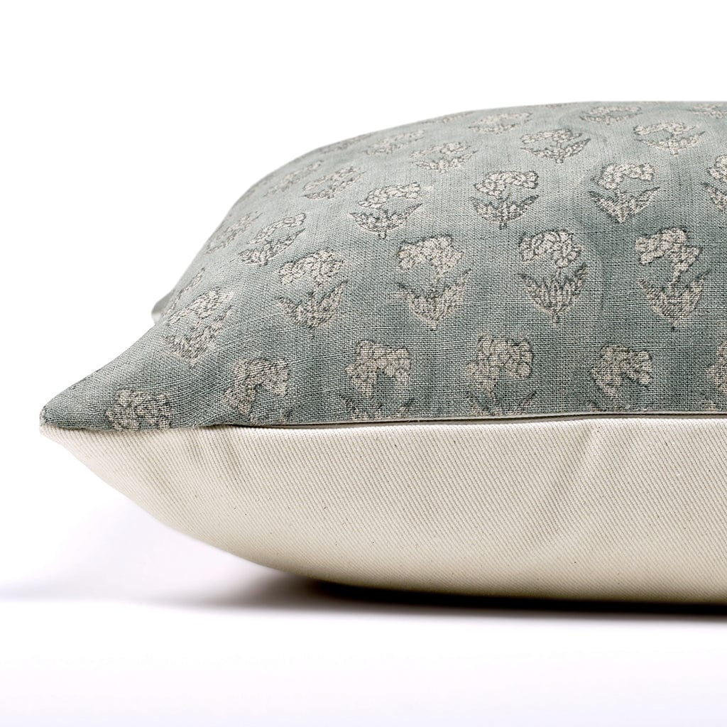 A close-up of a decorative pillow resting on its side, featuring a green hand block printed floral pattern on the top fabric and a plain beige linen pillow cover. The pillow appears soft and plush, lying on a white surface.