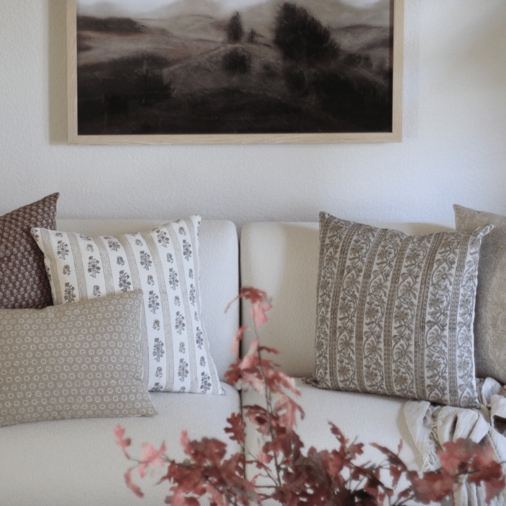 A cream sofa with Emery, Leighton, Isabelle, Louise and Matilda Lumbar in a living room with a wood coffee tale and large canvas behind the sofa