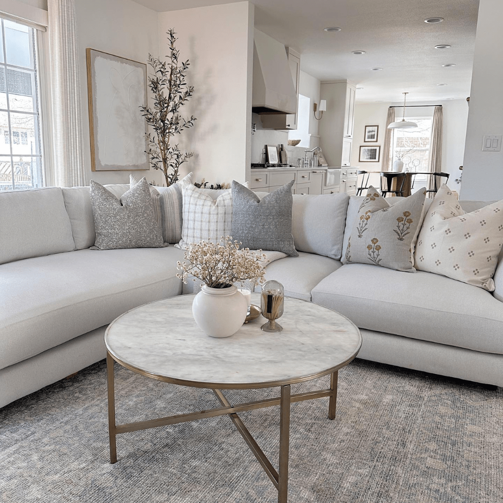 A couch covered in Colin + Finn pillows - Fitz, Felicity, Darby, Eloise, Remington, and Dara. Marble coffee table with gold frame in the center of the photo with a vase and flowers. 