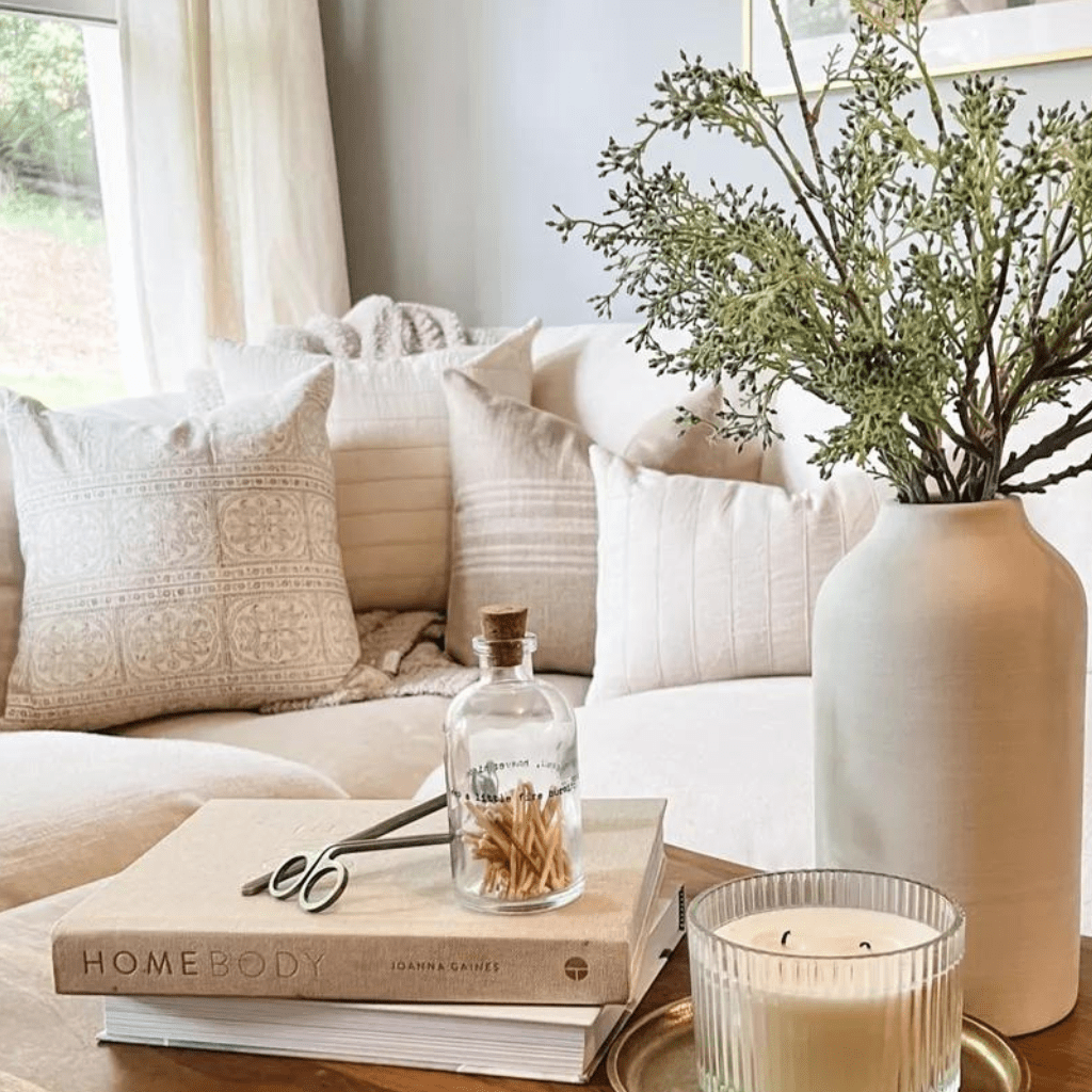 The corner of a couch with Karina, Logan, Kinsey, and Logan Lumbar. In the foreground is a coffee table with home decor books, matches, a candle, and a vase with flowers