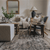 A living room with a side chair in the foreground with the Karina pillow and a beige couch in the background with the Neville Sand, Magnolia, and Elodie Lumbar pillows