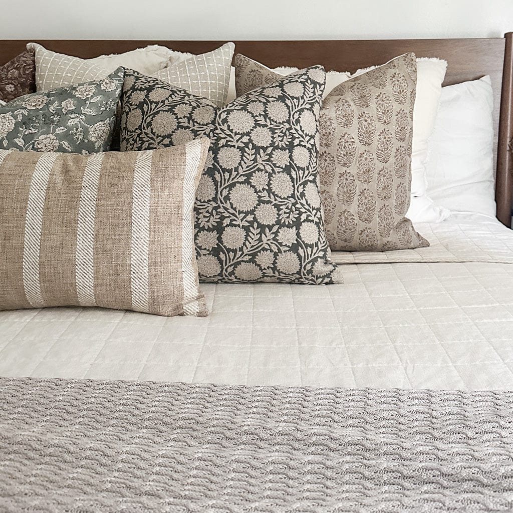 A neatly made bed with a wooden headboard, featuring Callum, Margot, Lenora, and Caspian lumbar pillow covers from Colin and Finn in neutral tones arranged against white bedding.