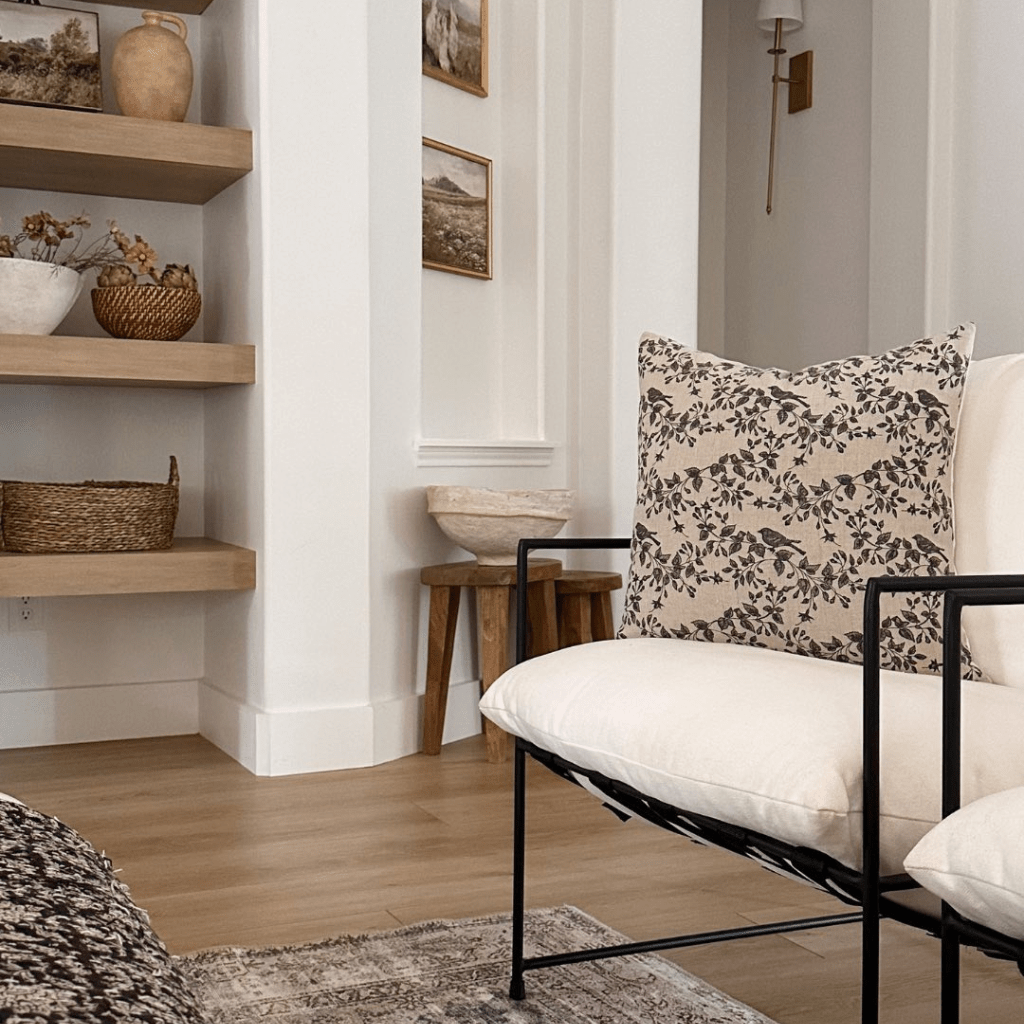 a Magnolia pillow from Colin+Finn sits on a chair to the right of the picture. On the left side of the photo are shelves with various vases and baskets