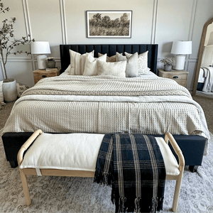 A bed with a black headboard covered in throw pillows and neutral blankets. Throw pillows are from Colin and Finn - Odin, Emberly, Delsi, Odette, Beatrice, and Logan Lumbar.